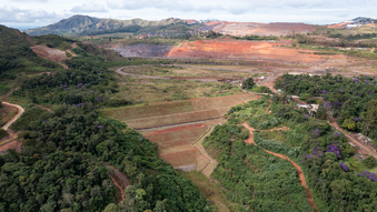 Imagem aérea da barragem Grupo. Há uma área montanhosa e diversas árvores ao redor e ao meio está a barragem, com vegetação rasteira. 