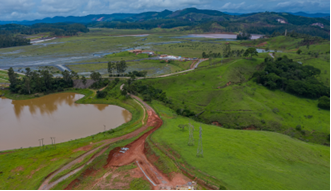 Foto vista de cima de uma vegetação baixa verde à direita da imagem e mais à esquerda uma parte de água e no meio um caminho de terra.