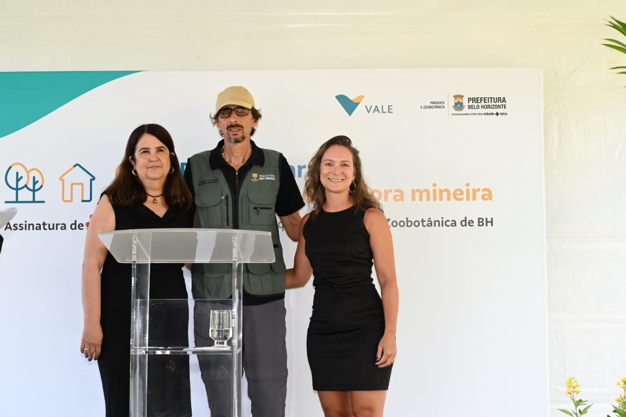 Duas mulheres vestidas de preto ao lado de um homem vestido de cinza. Os três estão a frente de um cartaz com o logotipo da Vale e atrás de um púlpito.