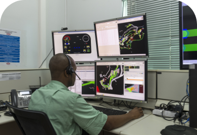 A man sitting in a chair in an office, wearing headphones and several monitors in front of him.