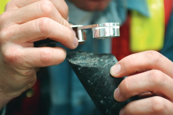 Mãos masculinas seguram matéria-prima do metal enquanto a observam através de lente de aumento detalhes da pedra. 